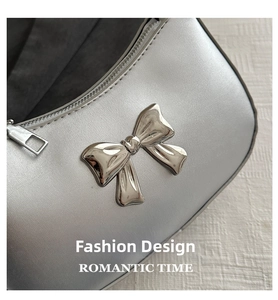 Detail of silver metallic handbag featuring a metal bow accent and smooth zipper