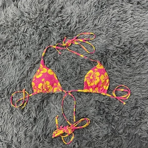 Detailansicht eines pinken Bikini-Oberteils mit gelbem Blumendruck und Schnürbändern