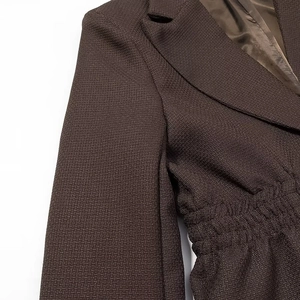 Detail of dark brown blazer with textured fabric and elegant pleated waist design