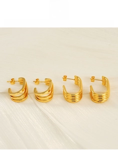 Detailed macro view of tiered gold titanium steel hoop earrings on white silk fabric