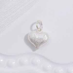 Detailed close-up of a silver heart pendant with fine textured scrollwork relief