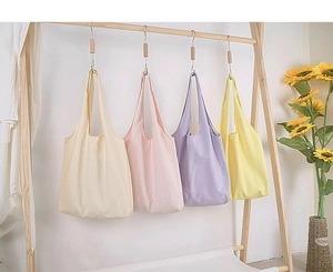Close-up of pastel canvas tote bags in beige, pink, purple, and yellow on wooden hangers