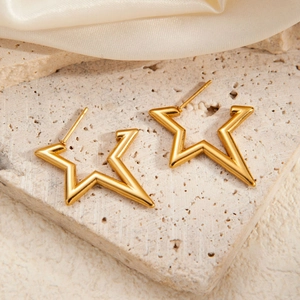Close-up of gold star-shaped stainless steel earrings on a beige stone base