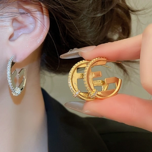 Detail of 18K gold-plated F-shaped earrings with zircon inlay worn by model