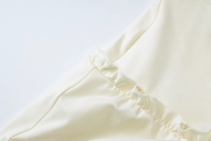 Close-up of cream white fabric texture with ruffle edges and precision stitching detail