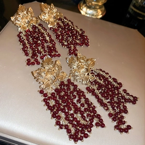 Detailed view of vintage gold leaf stud and deep red grape bunch beaded tassel earrings