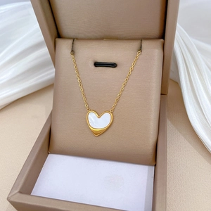 Detail of a gold heart necklace with a white shell inlay resting in a beige jewelry box