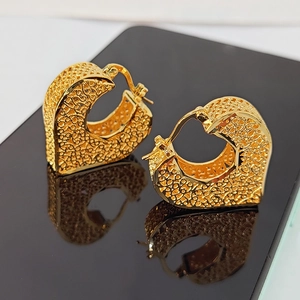 Golden heart-shaped filigree earrings with vintage hollow design on a reflective surface