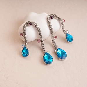 Detail of silver twisted metal drop earrings with blue teardrop crystal and colorful stones