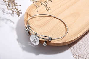 Detail of adjustable wire bracelet with engraved Love You Grandma heart charms on wood