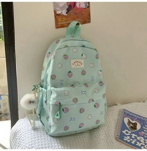 Detail of mint green strawberry backpack with plush pompom and heart patterns