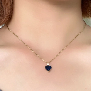 Close-up of heart-shaped blue zircon pendant on a gold chain necklace worn by a model