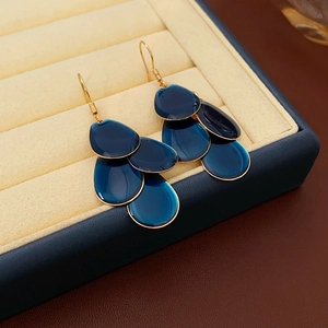 Close-up of blue scale tassel earrings with gold hooks on beige velvet jewelry box