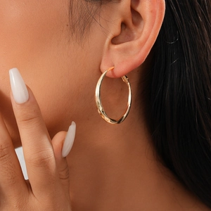 Close-up of model wearing gold circular metal hoop earrings with smooth polished finish