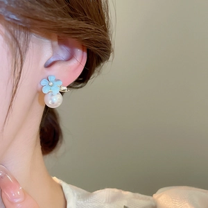 Detail of blue flower pearl earring on ear, showing delicate resin petals and metal base