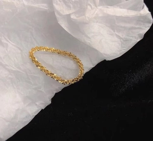 Close-up of gold chain ring with sparkling texture on white crumpled paper background
