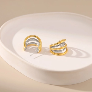 Minimalist spiral C-shape two-tone earrings in gold and silver on a ceramic tray