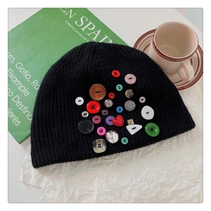 Close-up of black knit beanie with colorful decorative buttons on a cafe table background