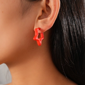 Close-up of matte red star-shaped C-style stud earrings worn on a model's ear