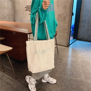 Detail of white canvas tote bag featuring blue smile embroidery and patterned shoulder strap
