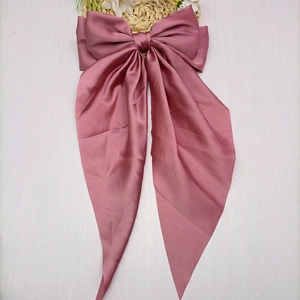 Close-up of elegant dusty pink satin bow hair clip with long ribbons on white wood