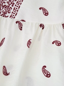 Detailansicht von weißem Stoff mit dunkelrotem Paisley-Muster und feiner Texturierung