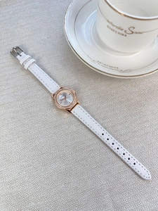 Detail of rose gold diamond-encrusted watch with white leather strap on woven fabric