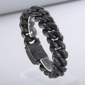 Close-up of vintage steel Cuban link bracelet with hammered texture on a clear stand