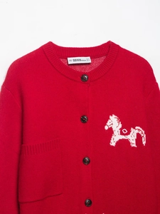 Détail d'un cardigan en maille rouge avec motif cheval blanc, col rond et boutons foncés