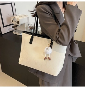 Grande borsa tote crema con bordi neri e ciondolo a mostro in un elegante ambiente caffè