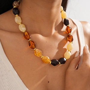 Detailed view of layered amber and beige acrylic beaded necklace on a female model