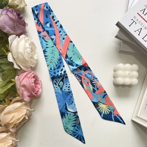 Blue tropical silk scarf with bird prints arranged with books and flowers detail