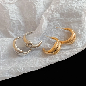 Detailed macro view of gold and silver layered C-shape teardrop earrings on art paper