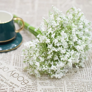 Detail of white artificial gypsophila bouquet on newspaper background with green cup