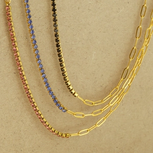 Detailed view of three gold necklaces featuring colorful zircons and asymmetric link chains