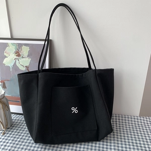 Detail of a thick black canvas tote bag featuring a front pocket and iconic white symbol