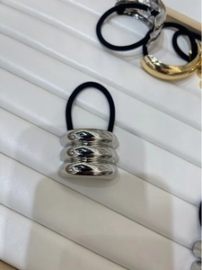 Close-up of a silver minimalist triple-ring hair tie on a white grooved display tray
