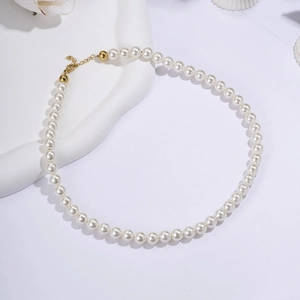 Detail of white pearl necklace with gold clasp on white stone background