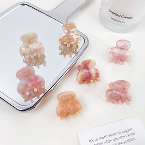 Mini pink acetate marble hair claws shown with elegant decorative props on white background