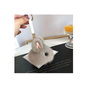 Plush grey rabbit head keychain with gold hardware and white strap shown against a book