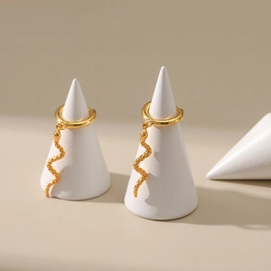 Minimalist gold snake hoop earrings with fine scale texture on white jewelry stands