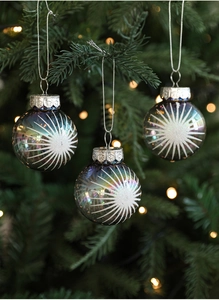 Iridescent Christmas ball with white glitter stars hanging on a festive pine tree branch