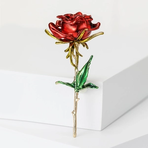 Elegant red enamel rose brooch with gold stem and green leaves on white background