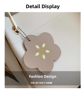 Detail of minimalist cream leather tote bag with a floral pendant and gold metal chain