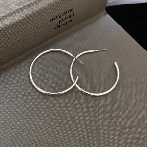 Detailed top view of minimalist silver hoop earrings with butterfly backs on grey surface