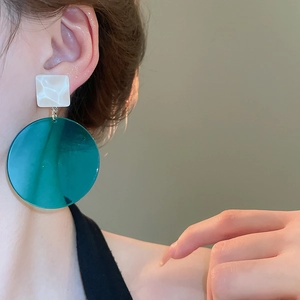 Detailed close-up of fashion geometric earrings with white square and green resin drops