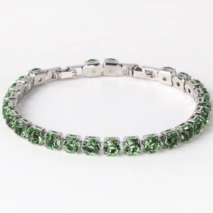 Macro detail of silver tennis bracelet featuring emerald green square-cut crystals