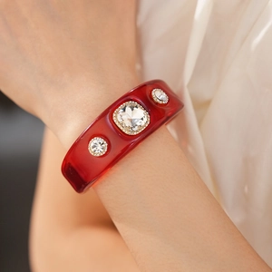 Macro detail of dark red resin bangle featuring crystal stones and pavé setting