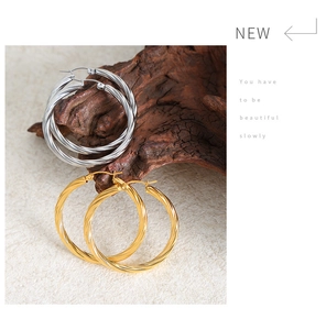 Detailed view of large gold and silver spiral hoop earrings on decorative wood