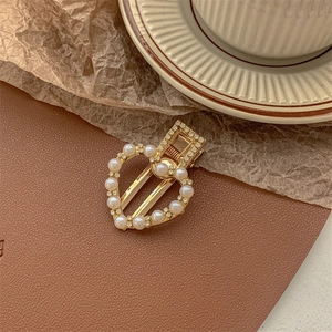 Detailed close-up of a golden heart-shaped hair clip with pearls and small rhinestones